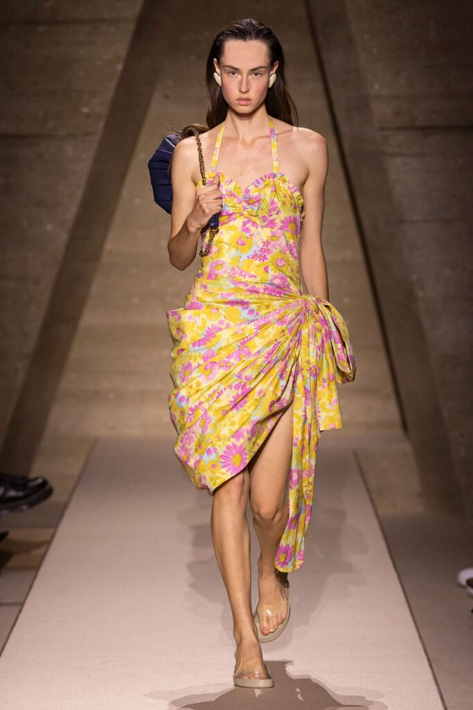 Model walks the Chloé Spring 2026 runway wearing the floral draped halterneck dress with oversized side bow.